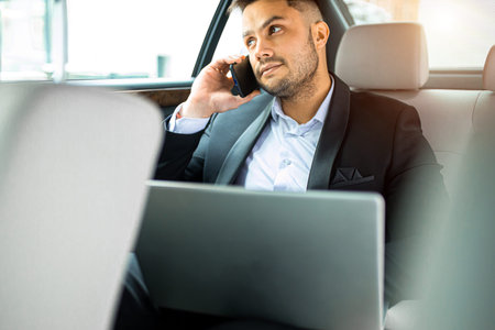 handsome young man sitting in his expensive car of top class, talking on phone and using laptop