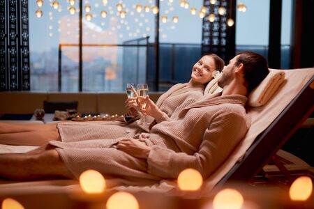 Spa, relax, enjoying concept. Married couple together relaxing in spa salon, lying on beds drinking champagne, using candlesの写真素材