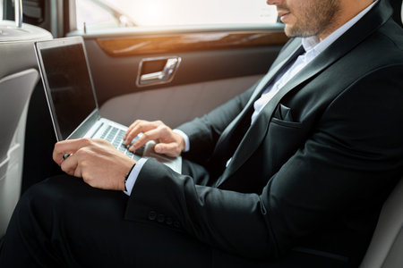 unrecognizable man wearing tuxedo use laptop in luxurious car, working.