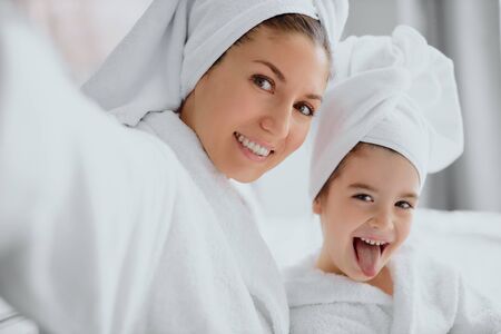 portrait of good-looking female wearing white bathrobe and towel sit looking at camera and smile.の写真素材