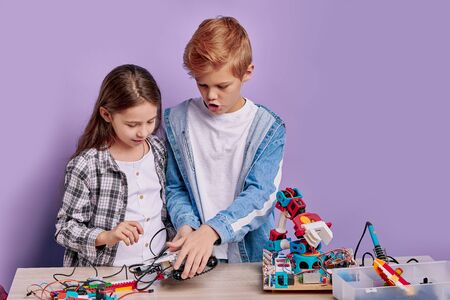 portrait of clever children assembling robots on table, teamwork, children involved in engineering, roboticsの写真素材