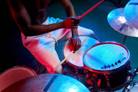 close-up of mans hands playing on drums, african man with skin in neon lightsの写真素材