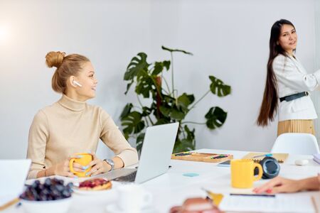 side view on modern young caucasian woman with headphones sit looking at speaker and laugh in office, use laptopの写真素材