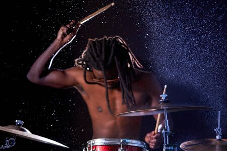 African drummer man musician hitting on wet drum cymbal and water splashing in slow motion isolated over dark backgroundの写真素材