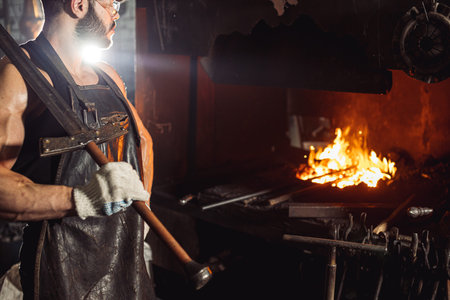 handsome muscular male blacksmith holding handmade metal for manufacturing, wearing leather apron or...