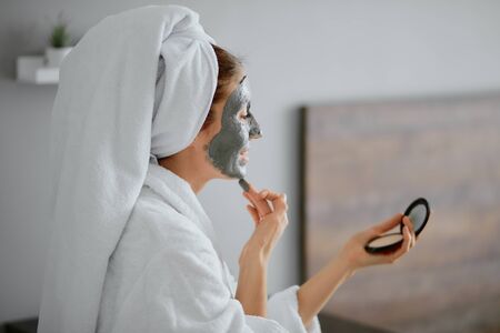 beautiful woman in bathrobe and towel apply facial mask, doing beauty procedures at home, healthcareの写真素材