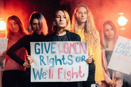 portrait of five angry feminists girls of caucasian appearance promoting feminism isolated in smoky space, holding posters with inscriptions like girls power, women rights, fighting for girls rightsの写真素材