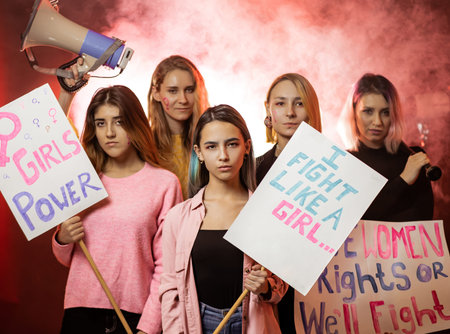 young beautiful women stand together in smoky space fighting for girls power holding posters