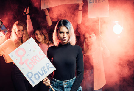 feminism concept. portrait of female holding poster on which girl power is written, wearing black...