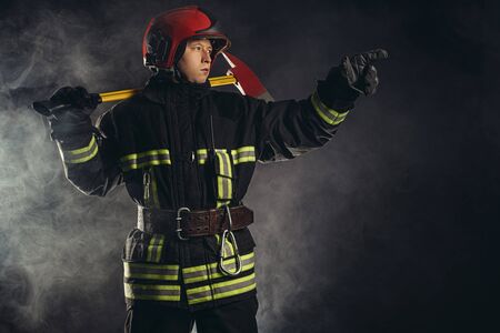young caucasian fireman show at fire, serious male in uniform gives a signal to colleagues working with him in fire station, emergency situationの写真素材
