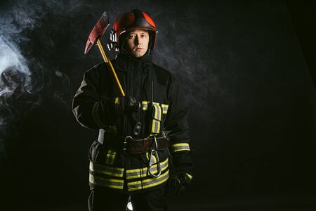portrait of serious and confident caucasian fireman stand holding hammer, wearing special protective uniform in the smoky backgroundの写真素材