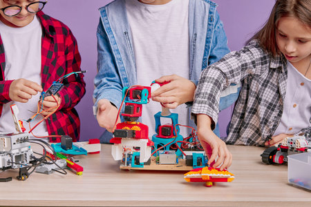 close-up robotics on table, three kids holding wires plastic toys, try to create new engineering...