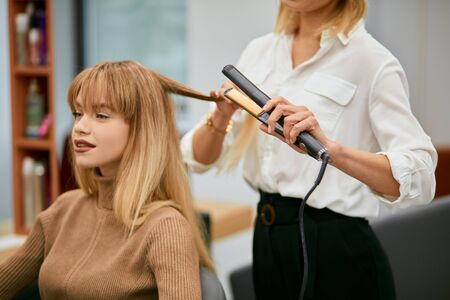 professional hair stylist making hairdo to young caucasian girl with long hair, careful hairdresser and young beautiful client in beauty saloonの写真素材