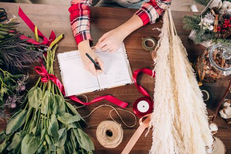 top view on young florist woman making notes at work, red ribbon, notebook and flowers lying on table. People, business, sale and floristry conceptの写真素材