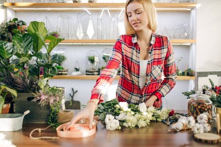 beautiful good-looking caucasian female florist make composition of flowers for customer, decorating bouquet, enjoy process of work around plantsの写真素材