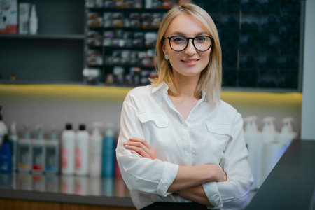 Portrait of smiling professional caucasian hairdresser looking at camera, wearing white formal shirt and eye glasses. Shampoos in the backgroundの写真素材