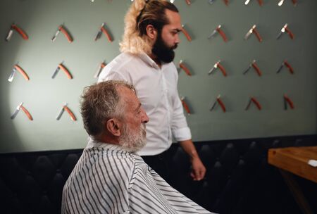 Old barber sitting at barber shop, close up side view portrait, man is preparing to cut his hait.lifestyle, free time, spare timeの写真素材