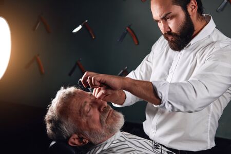 skilled barber enjoying his work at barbershop. close up side view photoの写真素材