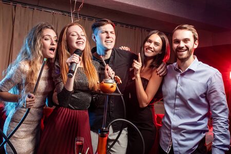 group of young caucasian people in party clothes have free time. leisure time in karaoke bar, enjoy singing, drinkingの写真素材