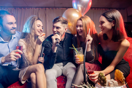 group of young people together in karaoke bar, singing and having fun together, clubbers rocking and...