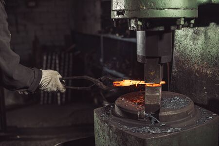 close-up of folding metal by blacksmith wearing protective gloves. cropped man holding ironの写真素材