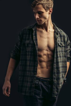 portrait of fit caucasian man with muscular body in checkered shirt with naked torso isolated over black backgroundの写真素材