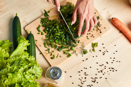 Studio shot of female hands making vegetarian salad, cutting scallions on wooden board, cooking at...