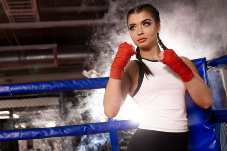 Strong muscular woman boxer ready to fight with enemy in ring, wearing red bandage on wrists, woman...