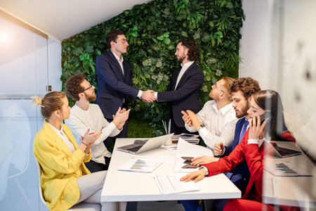 young business people shaking hands after successful conclusion of a treaty while other colleagues...