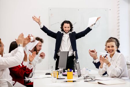 happy and cheerful business team happy after successful realization of project, celebrating in light office, boss congratulate, raised hands from happinessの写真素材