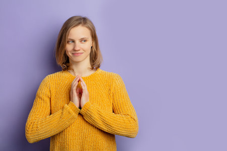 portrait of young caucasian funny girl conceiving something, look tempting isolated over purple background, wearing yellow blouse and looking sideの写真素材