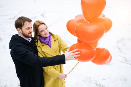 romantic date or anniversary of couple walking, spending time together at winter street. man and woman happy together, hold red air balloons in hands. celebration of saint valentines day. love conceptの写真素材