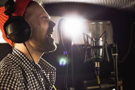 handsome caucasian guy in recording studio. young man professional singer preparing before music performance, concert. man warms up the vocal cordsの写真素材