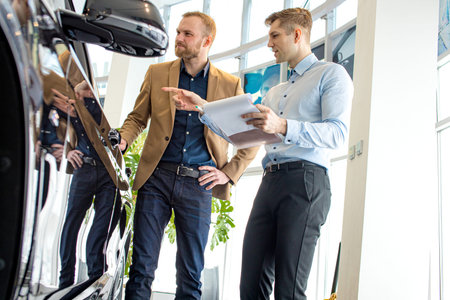 young caucasian cars salesman show the best variant to customer in dealership. handsome business man...