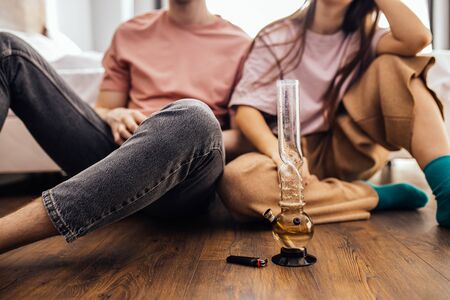 caucasian couple catch a buzz from using cannabis, marijuana. man and woman enjoy using drugs together, they warm bong with cannabis and smoke it. drugs treatment, ganja and hemp medicine conceptの写真素材