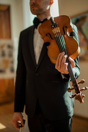 young caucasian male holding violin in hands, man going to play violin, perform classic music. professional musician before his concertの写真素材