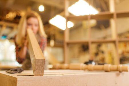 professional young carpenter lady examining wooden piece after grinding, woman make perfect handicraftの写真素材
