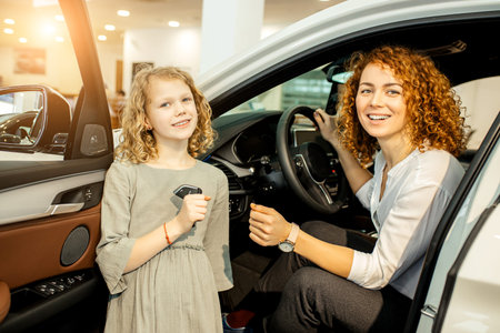 young caucasian owners of new automobile. mother and daughter came to get new car in dealership,...