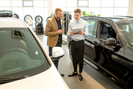 handsome young caucasian cars salesman help customer with choose. man came to get new car, looking...