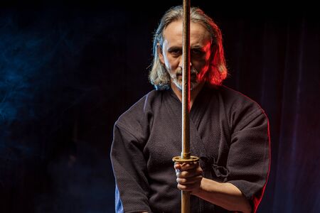 confident strong mature kendo warrior with shinai in hands, preparing for kendo competitions, fighting. isolated dark spaceの写真素材