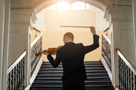 rear view on young caucasian male in elegant stylish suit playing violin in opposite of stairs....