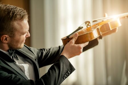 young caucasian professional male violinist studying and checking violin strings before concert. man hold new violin in hands and look at itの写真素材