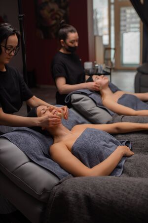 beautiful caucasian women get skin treatment, face lift by professional masseurs in wellness beauty salon. attractive ladies are pampered at the health spaの写真素材