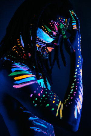 fantastic mysterious african male with UV body art posing at camera, futuristic body art, fluorescent paints glows in neon lightの写真素材