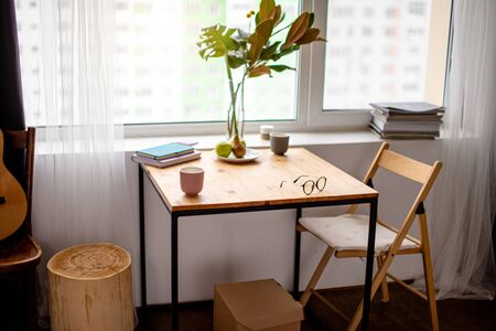small wooden table at home, modern compact kitchen table. green plant, a cup of coffee and eyeglasses on tableの写真素材