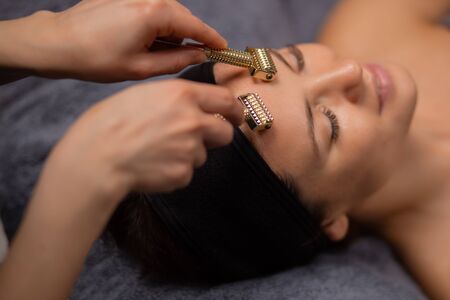 masseur use jade roller for facelift, cosmetologist drives tool on forehead for getting smooth skinの写真素材