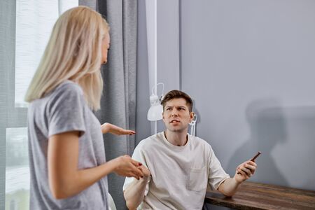 how much can you sit with the phone, dissatisfied woman and lazy man argue at home, man sit using mobile phone, lazybonesの写真素材