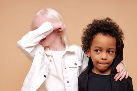 portrait of black afro and albino kids at a loss, girl with unusual appearance closed her eyes with hands and multiracial boy sadly looking side, isolatedの写真素材