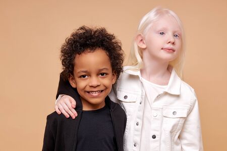 close friendship between two children of different nationalities, beautiful caucasian albino girl and dark-skinned african boy with curly hair, they are huggingの写真素材