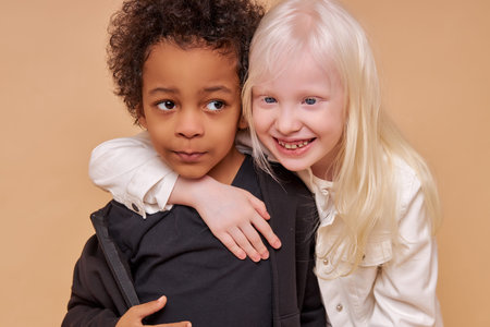 two friendly multiracial children stand together isolated over beige background, diverse positive...